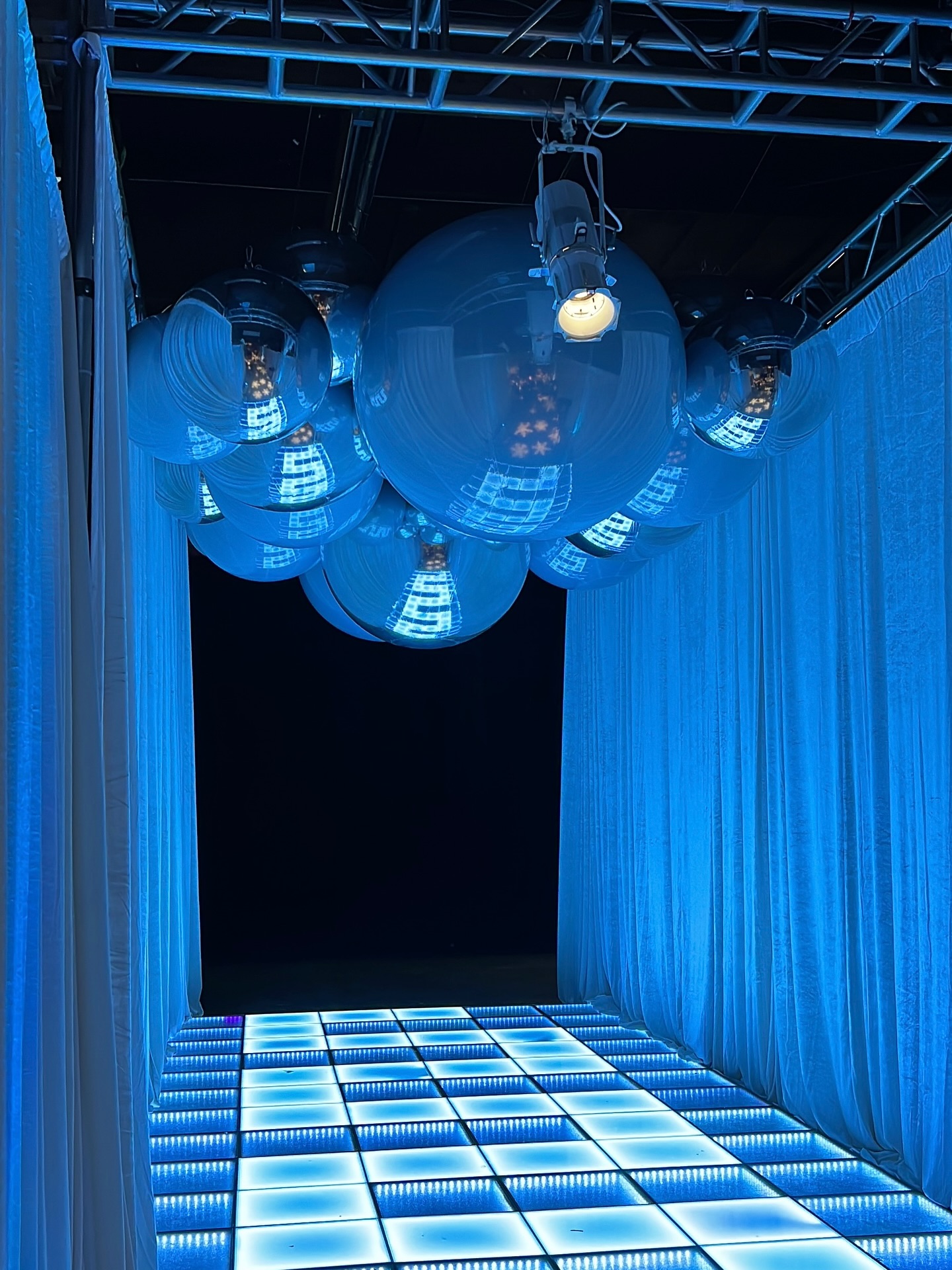 Cloud of mirror spheres hanging over a blue-lit infinity dance floor framed by white drape