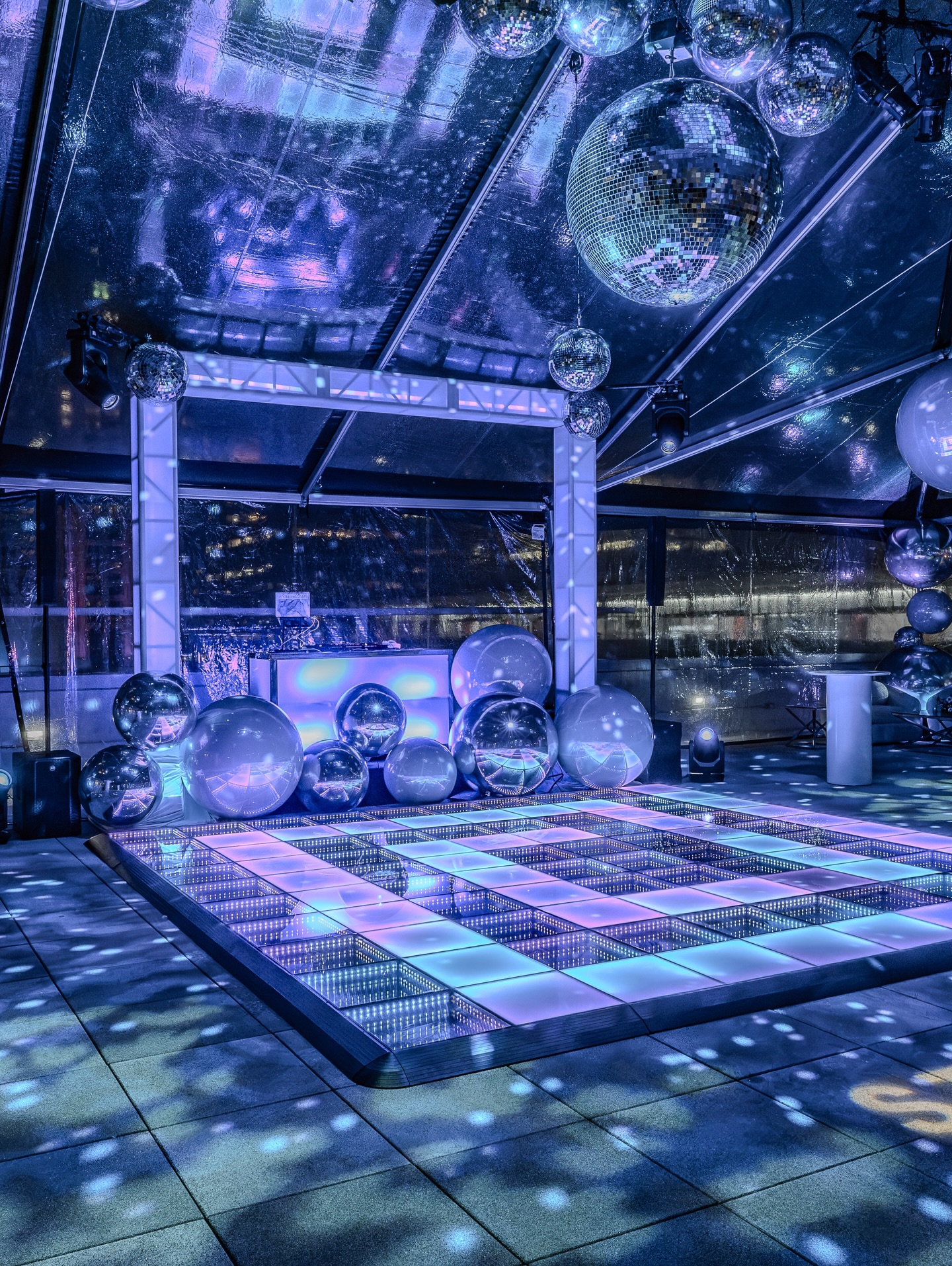 Pastel-lit infinity dance floor and mirror spheres in a rooftop tent with city views