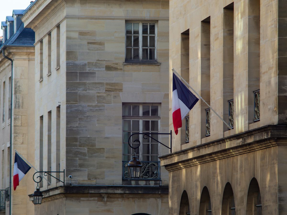 Façade en pierre d'un bâtiment public français ornée de drapeaux tricolores, à l'image des mairies où se déclarent les meublés de tourisme pendant la transition.