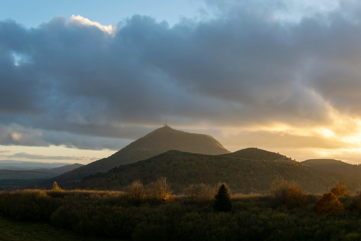 Le puy de Dôme et les volcans de la chaîne des Puys au coucher du soleil, sous un ciel nuageux, dans le département où les chambres d'hôtes Driing sont les plus nombreuses.