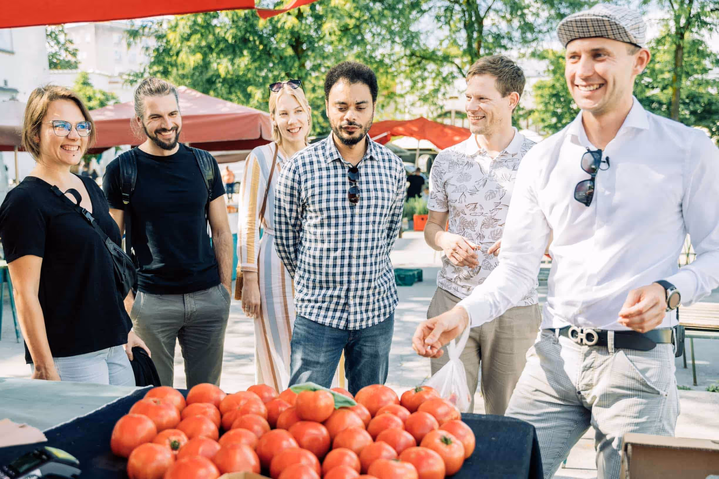 Food Tour group smiling and browsing fresh tomatoes at Ljubljana Central Market