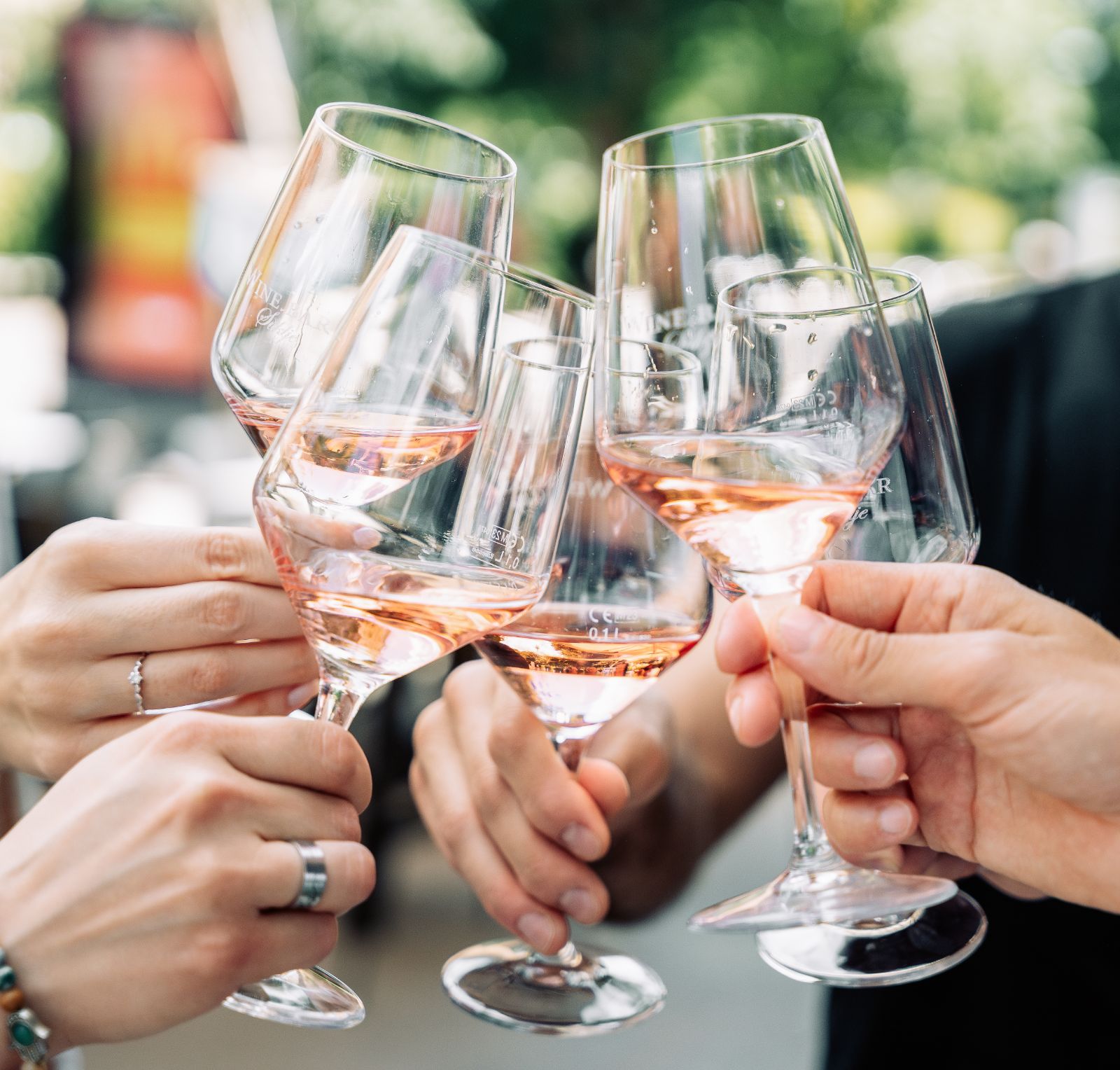 A group of friends clinking glasses of rosé wine outdoors on a sunny day.