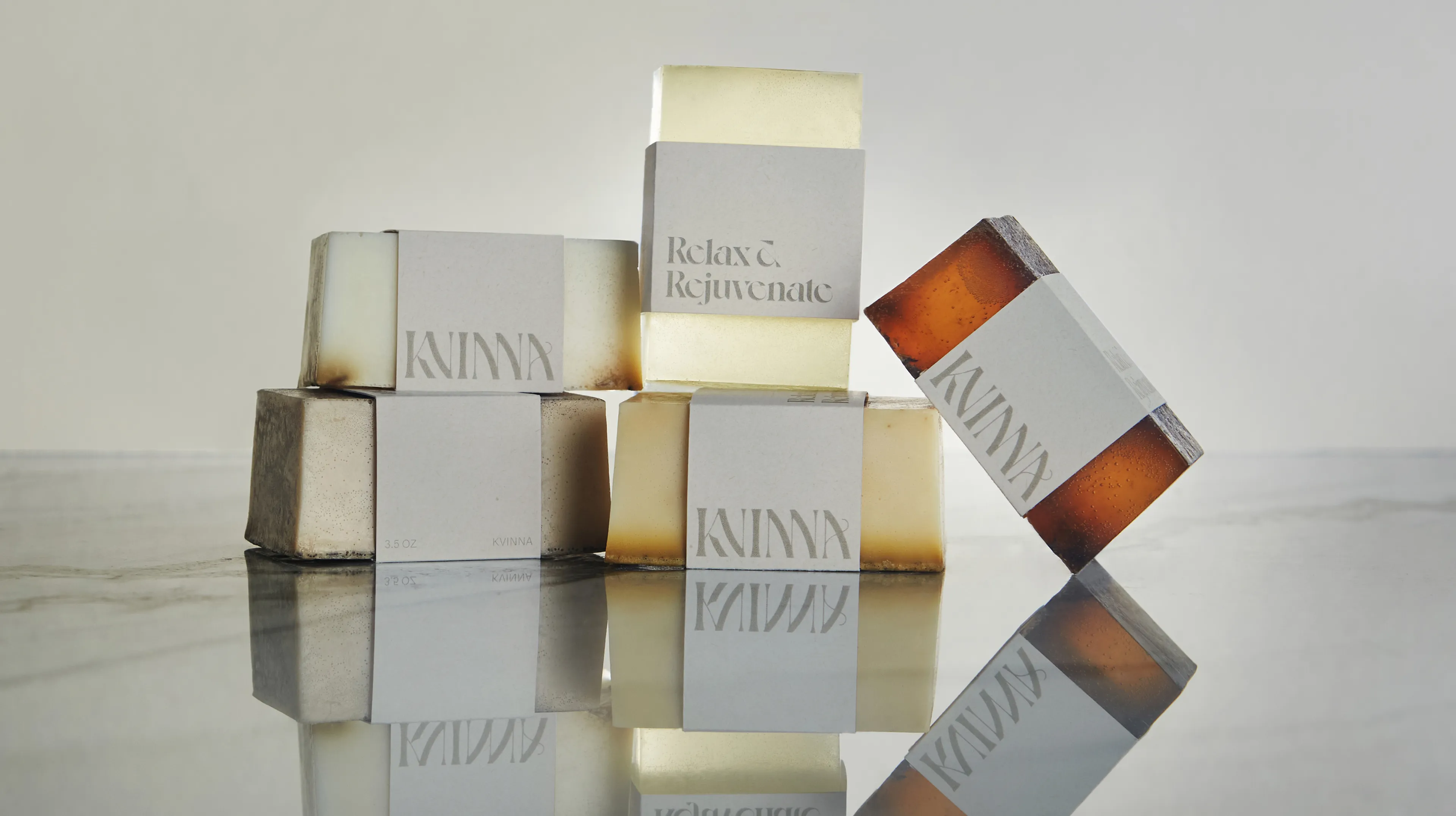 Kvinna branded artisan soap bars in translucent amber and cream tones with 'Relax & Rejuvenate' label, arranged on reflective marble surface, designed by Unbound Collective