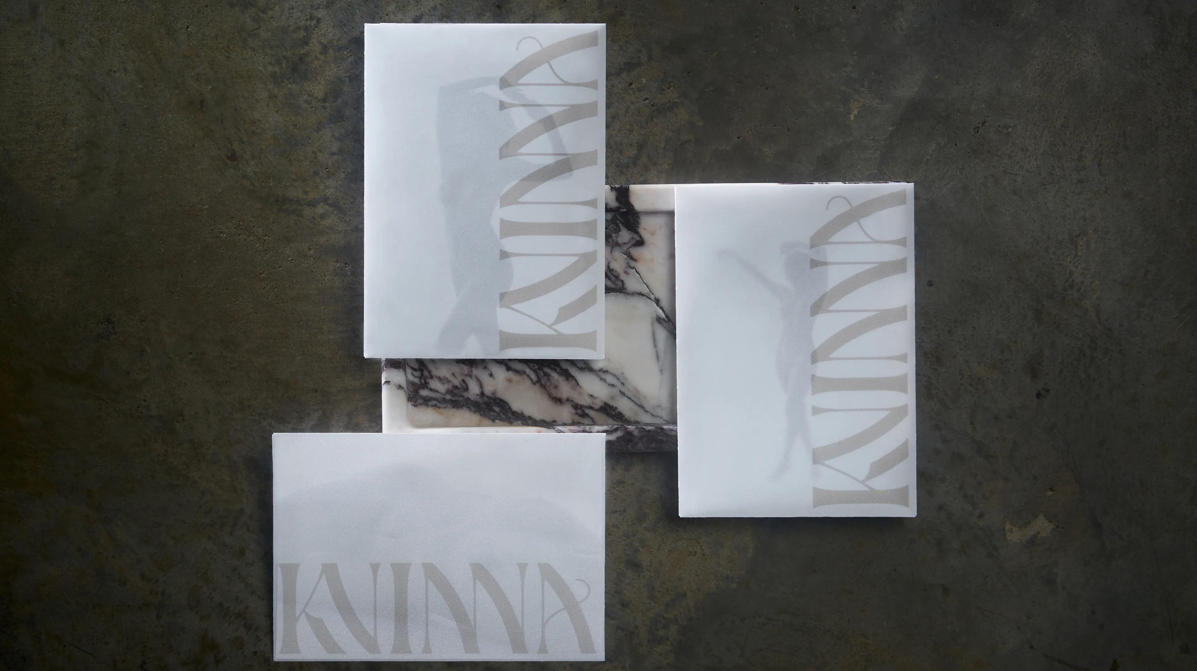 Kvinna branded white stationery cards with serif logo arranged in flatlay on dark marble surface with veining, brand identity designed by Unbound Collective