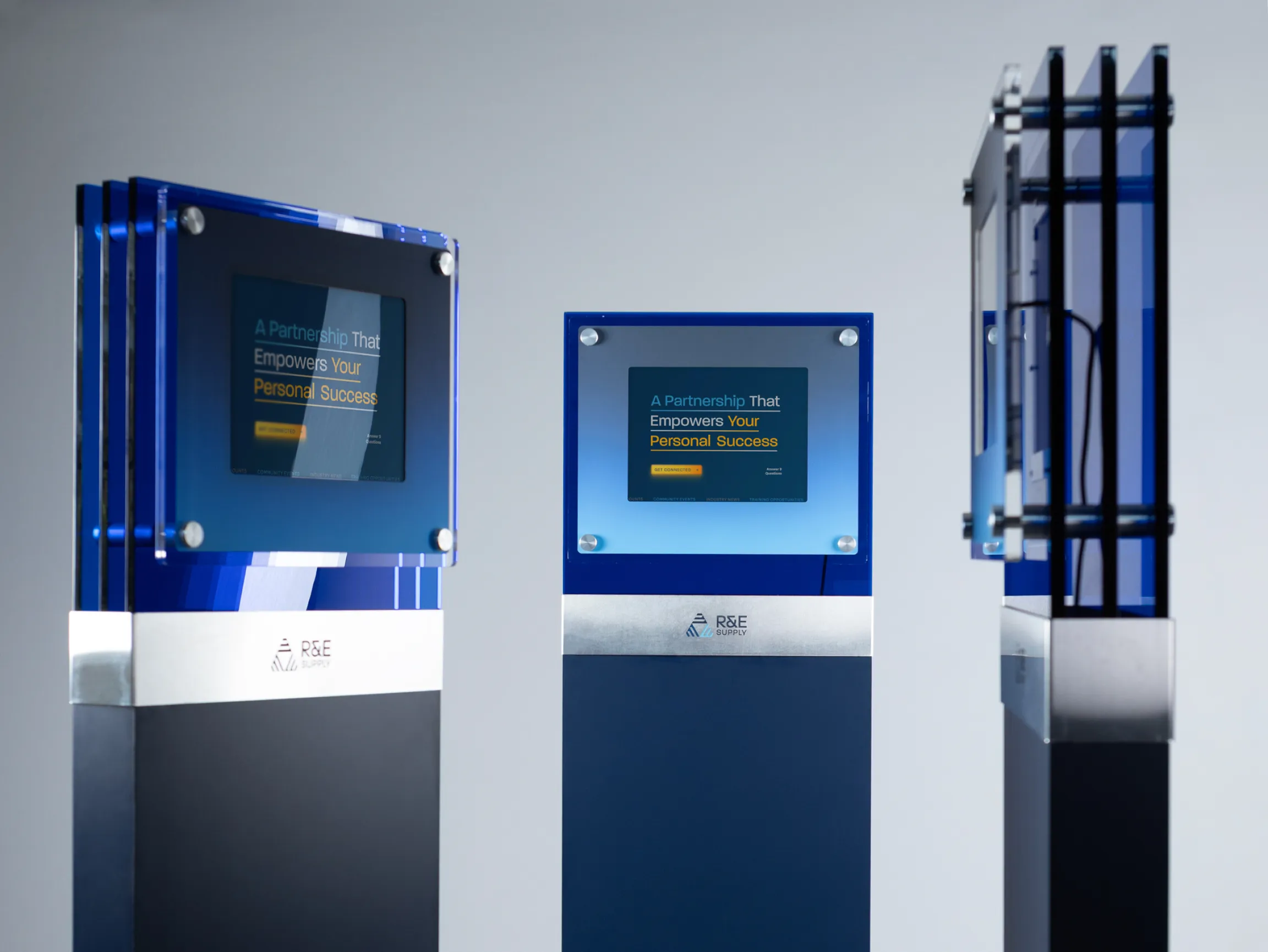 R&E Supply interactive kiosk with blue acrylic display panels designed by Unbound Collective, featuring 'A Partnership That Empowers Your Personal Success' screen