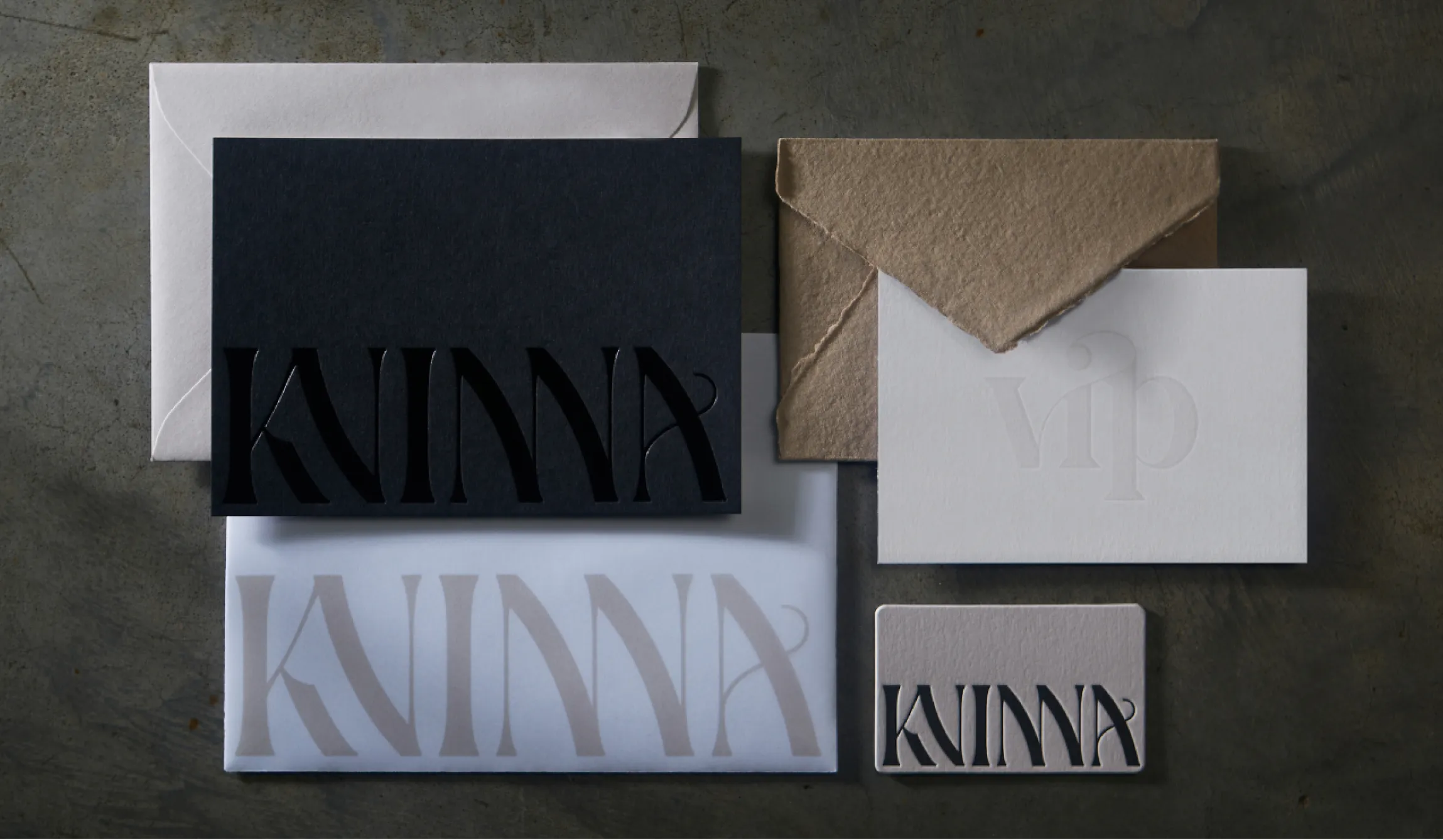 Kvinna Studio brand stationery flatlay showing black embossed card, white VIP card, kraft envelope, lavender envelope, and rounded business card with display serif logotype, brand design by Unbound Collective