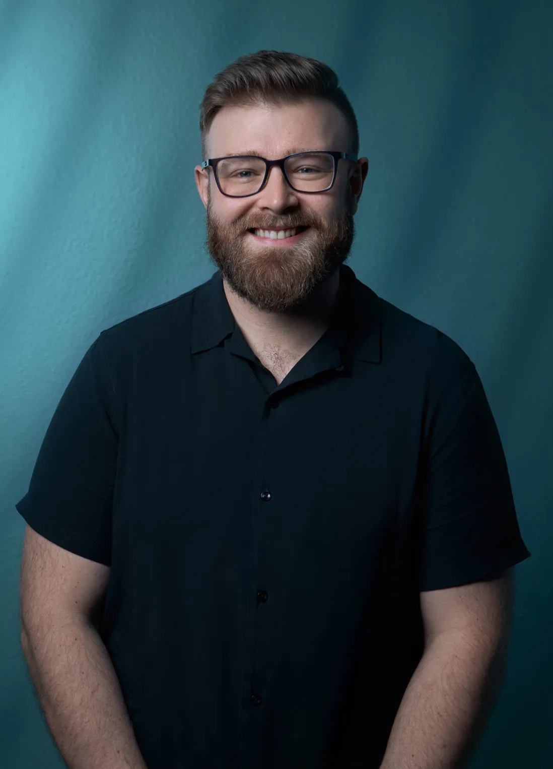 Tyler Bushong of Bushong Accounting professional headshot in a dark button-up shirt and glasses against a teal studio background by Unbound Collective