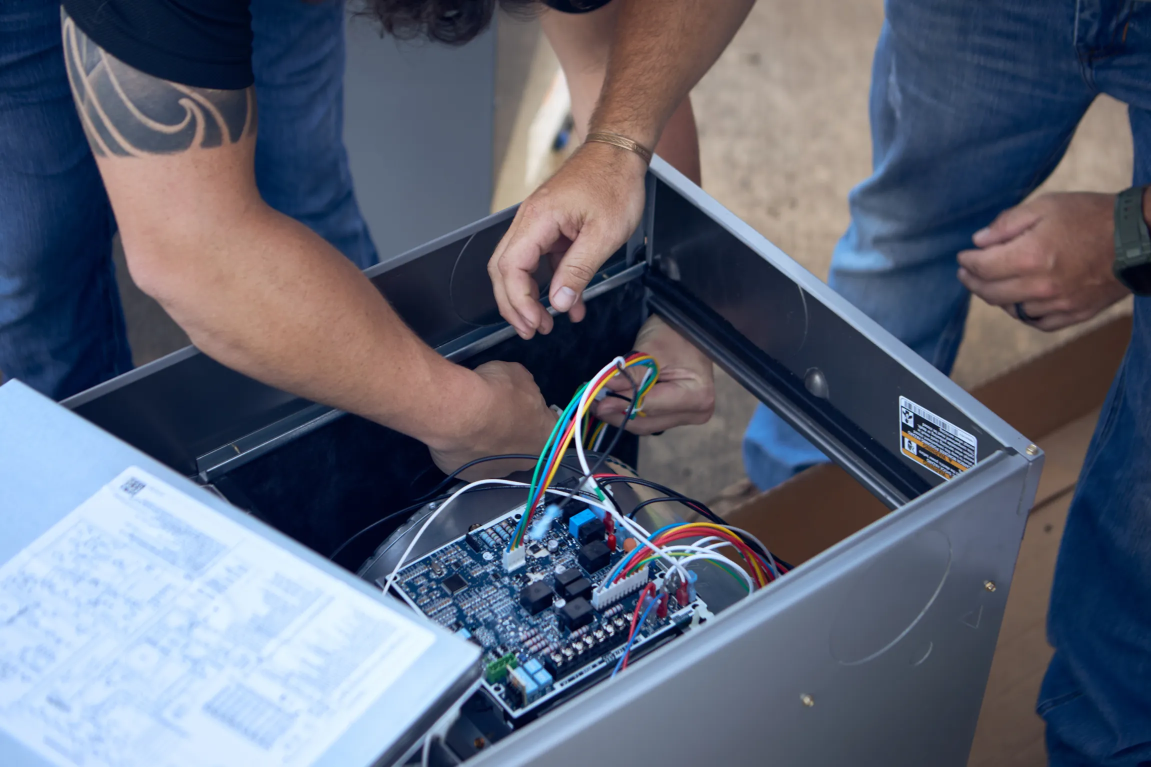 Ski Brothers HVAC technician with tattoo sleeve routing wiring inside an open HVAC control unit during installation by Unbound Collective