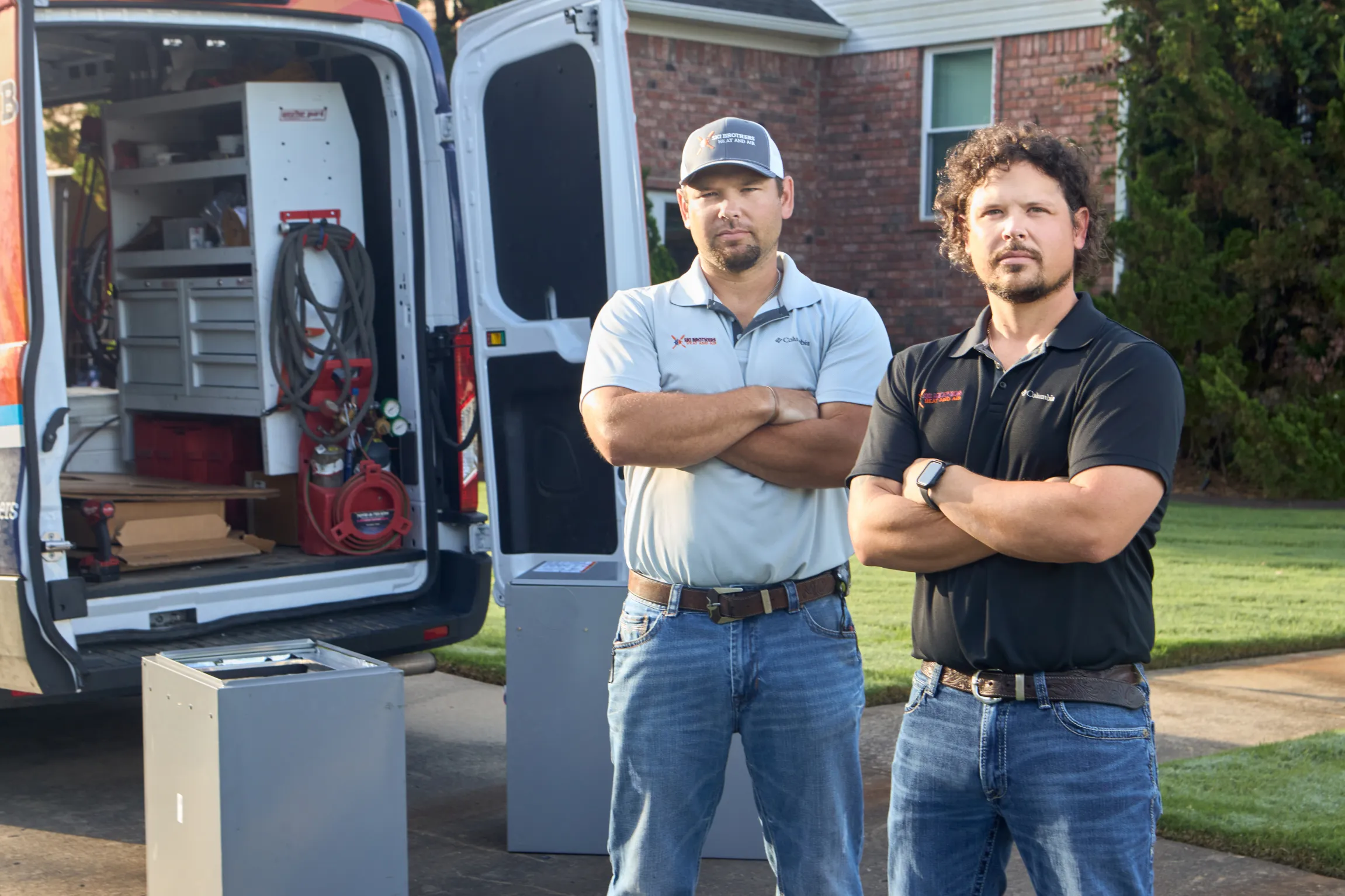 Two Ski Brothers HVAC owners standing arms crossed in front of their open service van at a residential job site by Unbound Collective