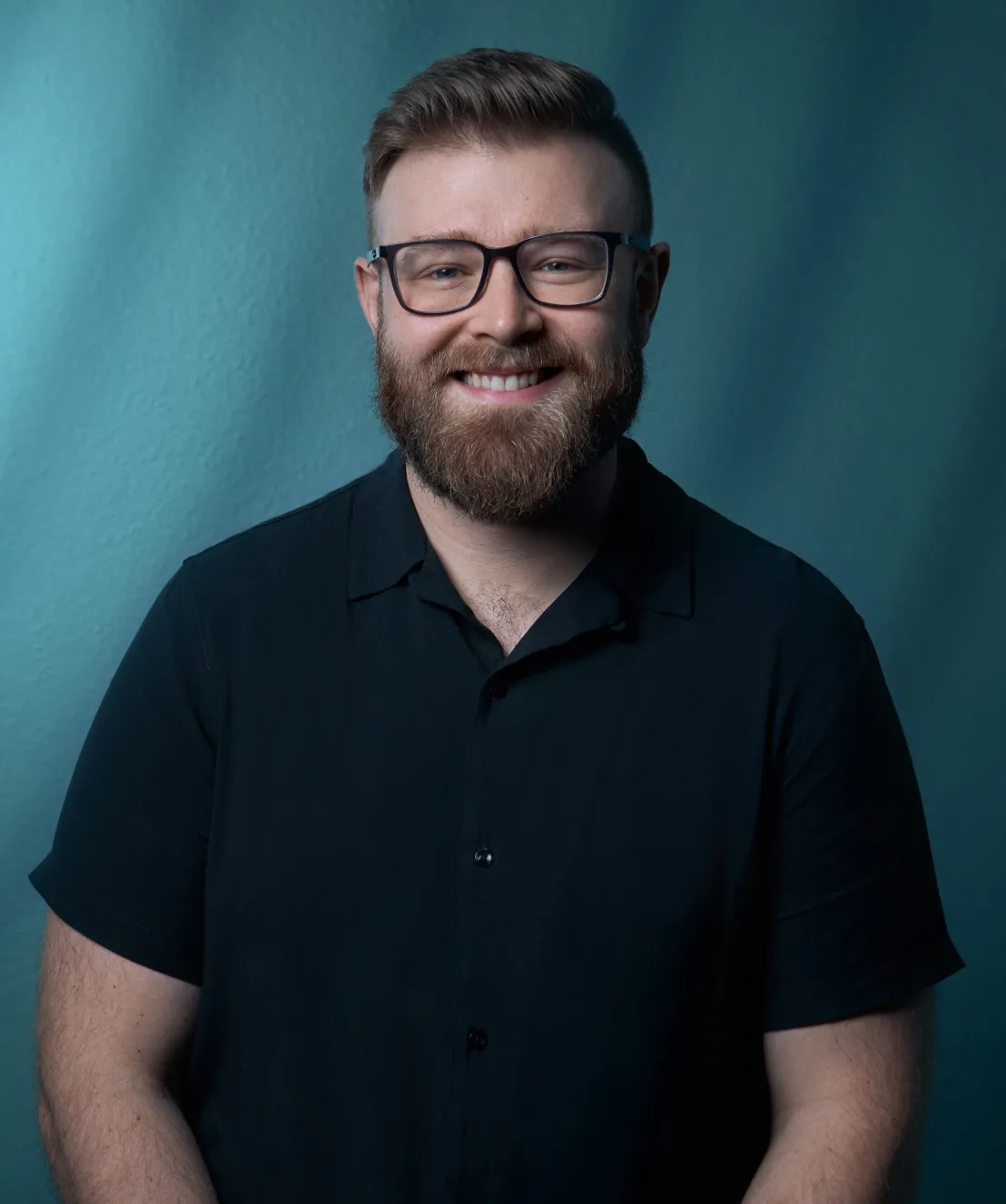 Tyler Bushong of Bushong Accounting professional headshot in a dark button-up shirt and glasses against a teal studio background by Unbound Collective