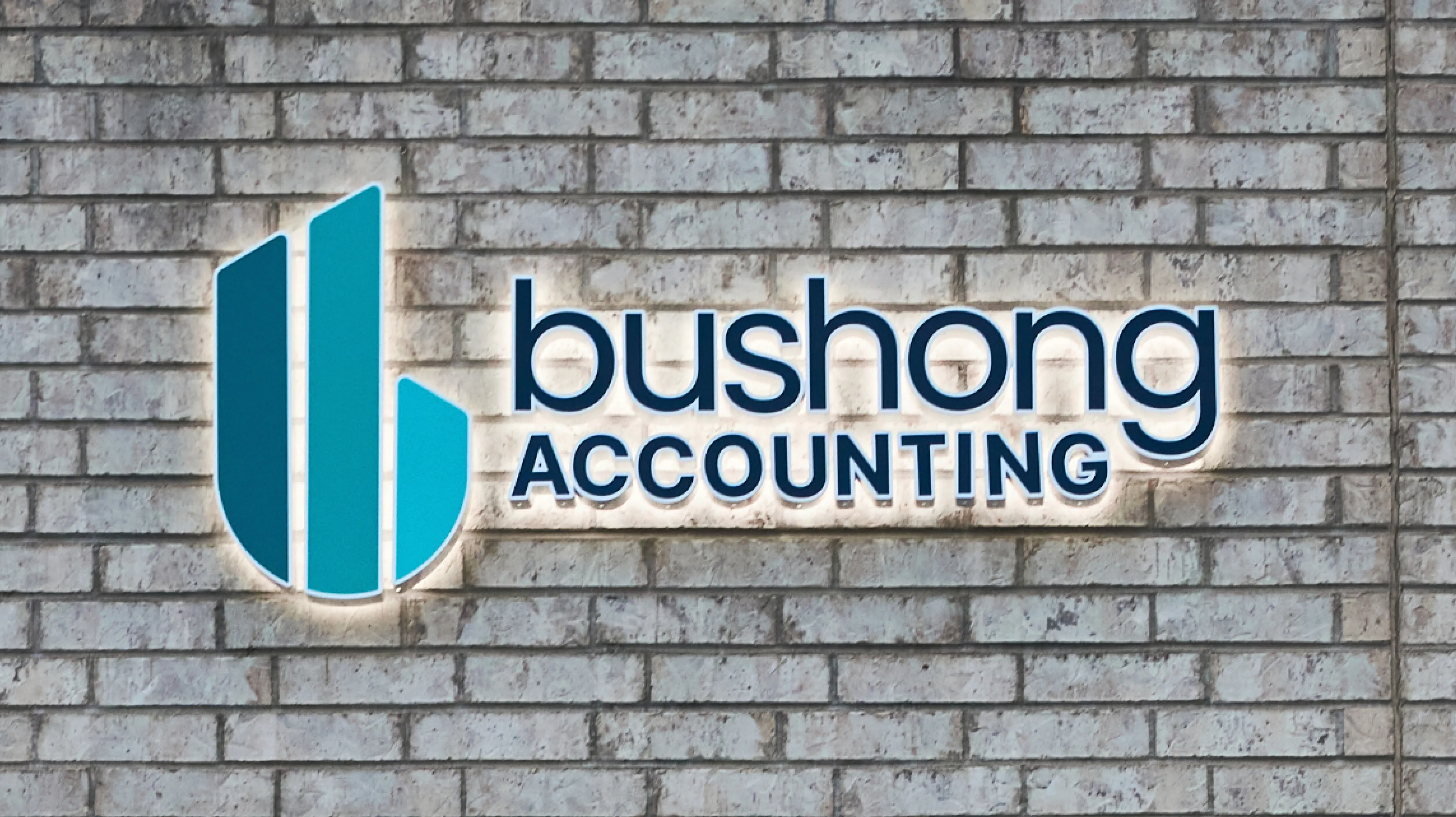 Bushong Accounting backlit dimensional logo sign mounted on white brick exterior wall, environmental signage by Unbound Collective
