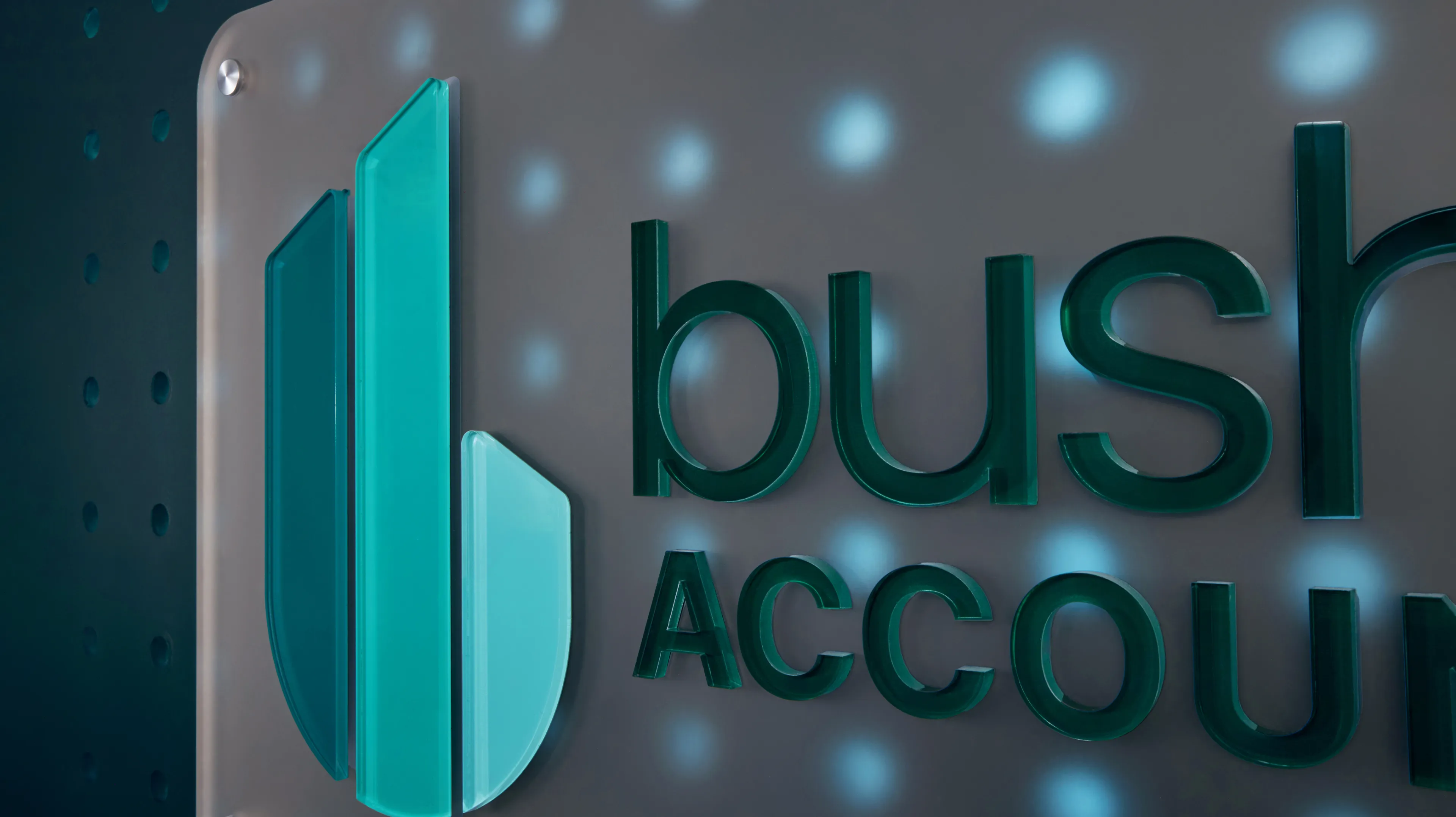 Bushong Accounting 3D logo sign closeup showing teal acrylic letterforms and icon on brushed metal panel with glowing dot detail, environmental signage by Unbound Collective
