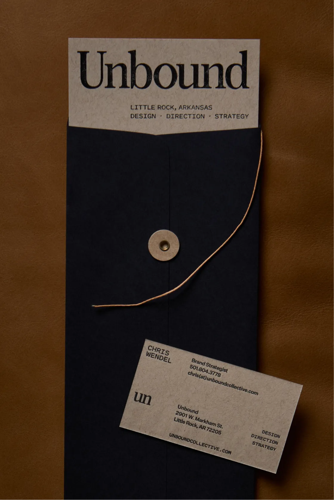 Unbound Collective branded navy string-tie envelope with kraft business card on a brown leather surface, print design and brand identity by Unbound Collective