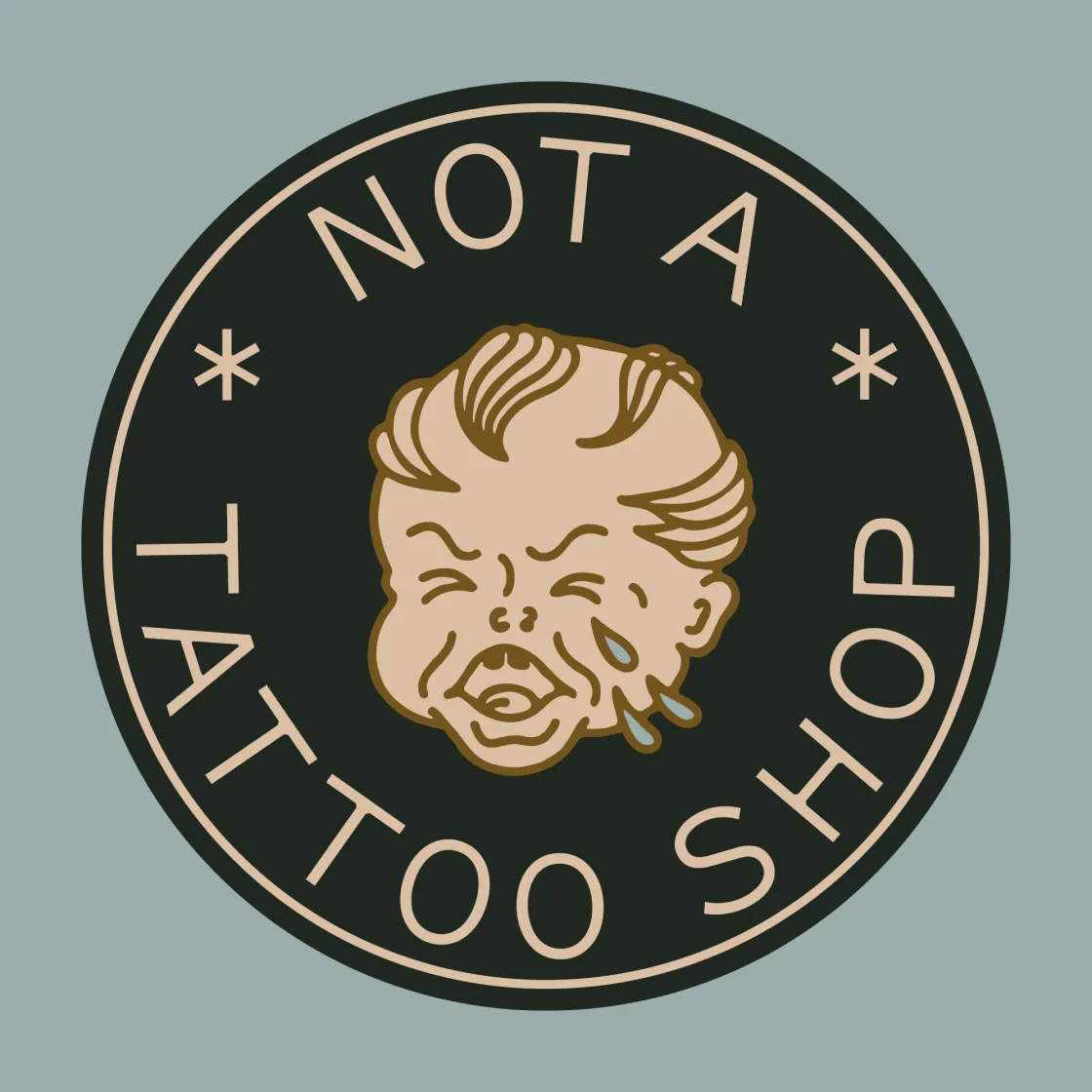Unbound Collective "Not a Tattoo Shop" circular badge with crying baby mascot illustration in dark green and sand on slate blue background, brand identity design by Unbound Collective