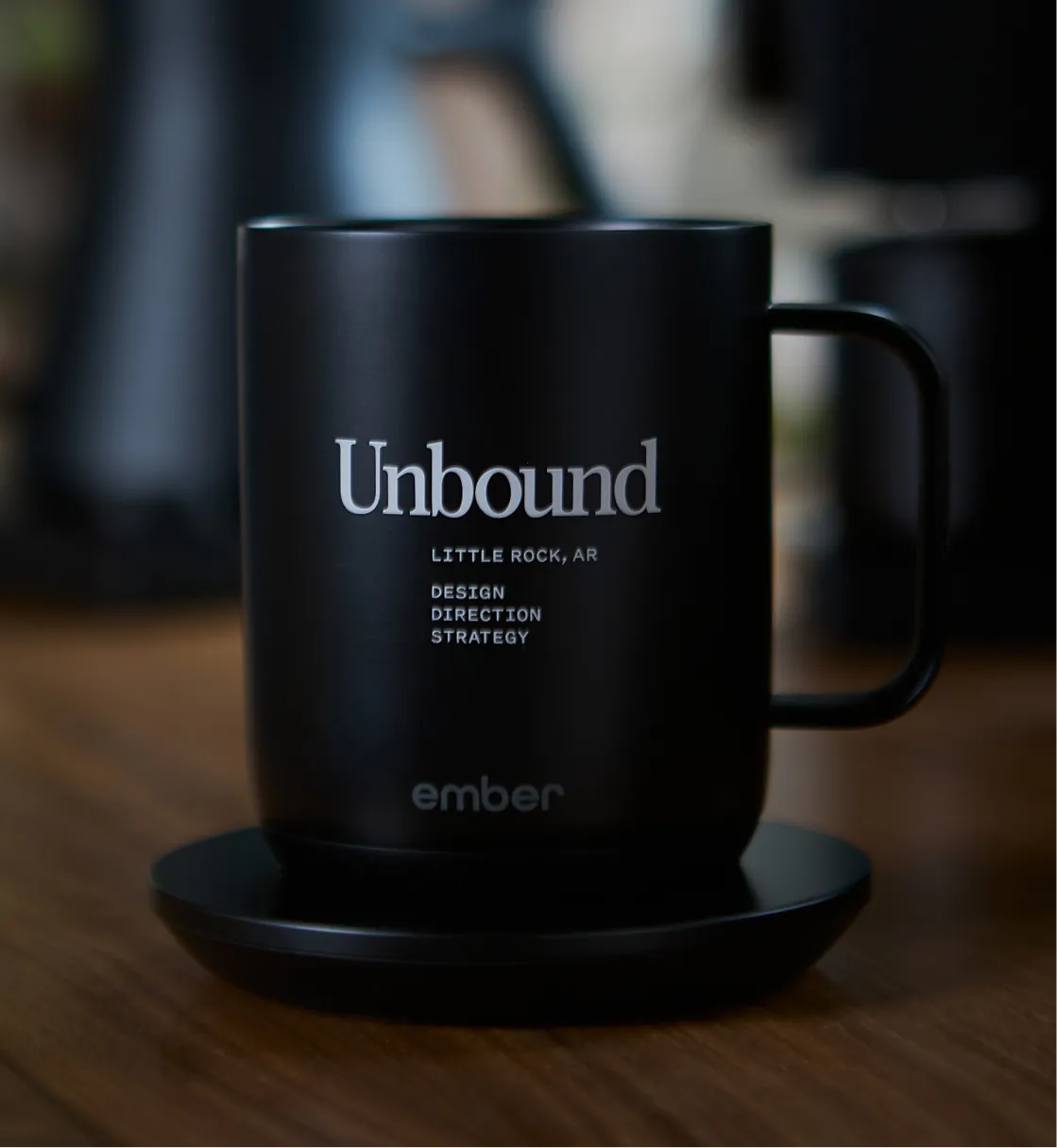 Unbound Collective branded black Ember smart mug with wordmark and tagline on wooden surface, brand identity and merchandise design by Unbound Collective