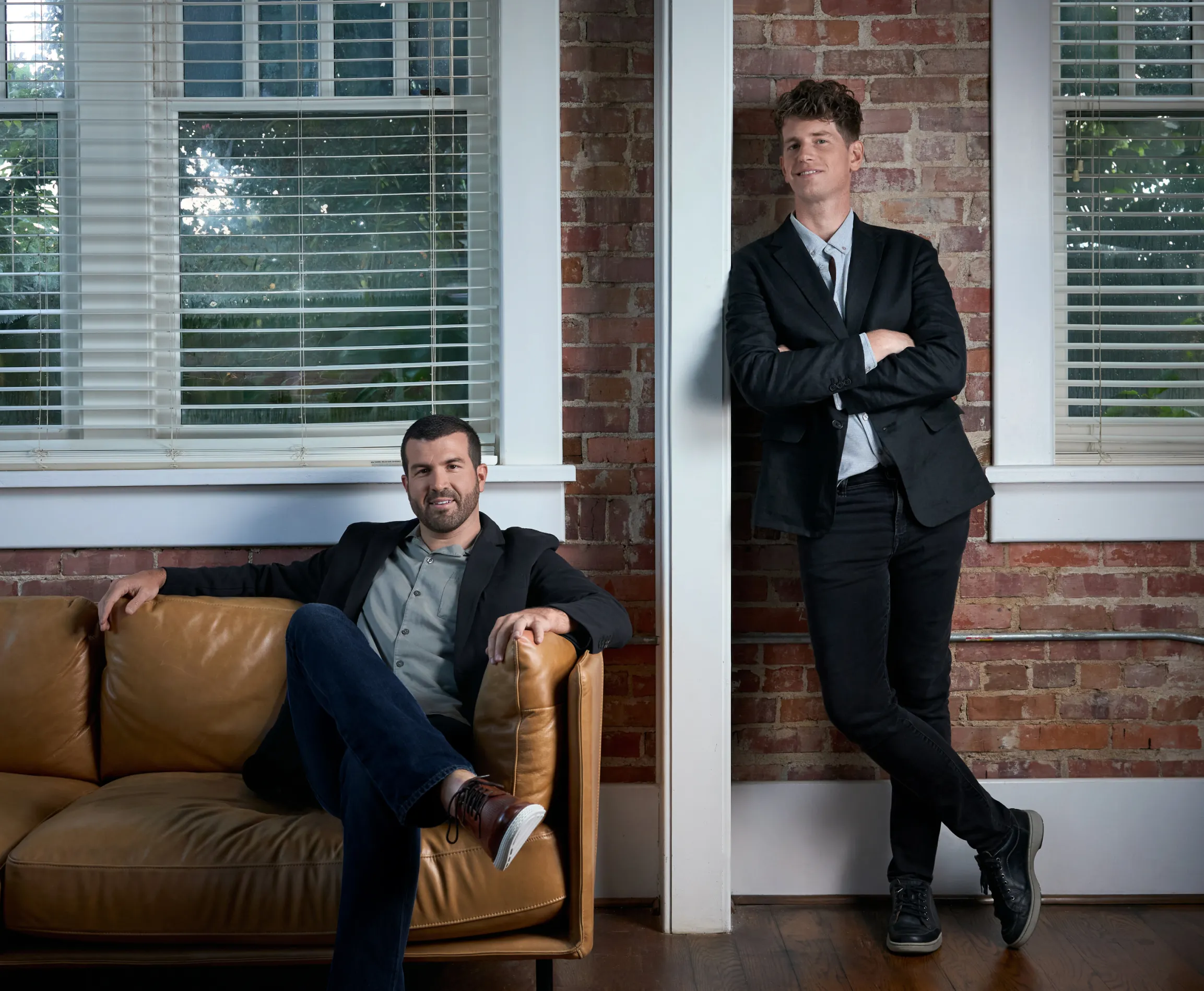 Unbound Collective founders Chris Wendel seated on a leather sofa and Hunter Oden leaning against a brick wall in the studio, brand photography by Unbound Collective