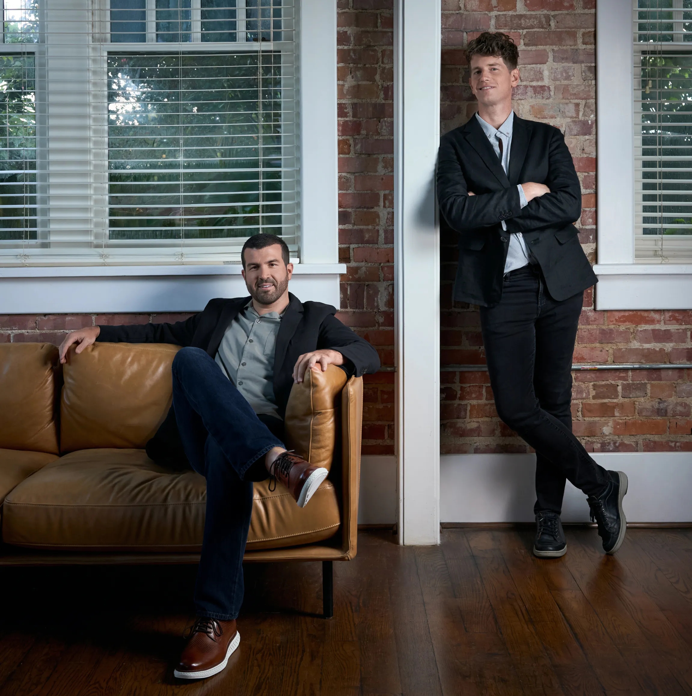 Unbound Collective founders Chris Wendel seated on a leather sofa and Hunter Oden leaning against a brick wall in the studio, brand photography by Unbound Collective