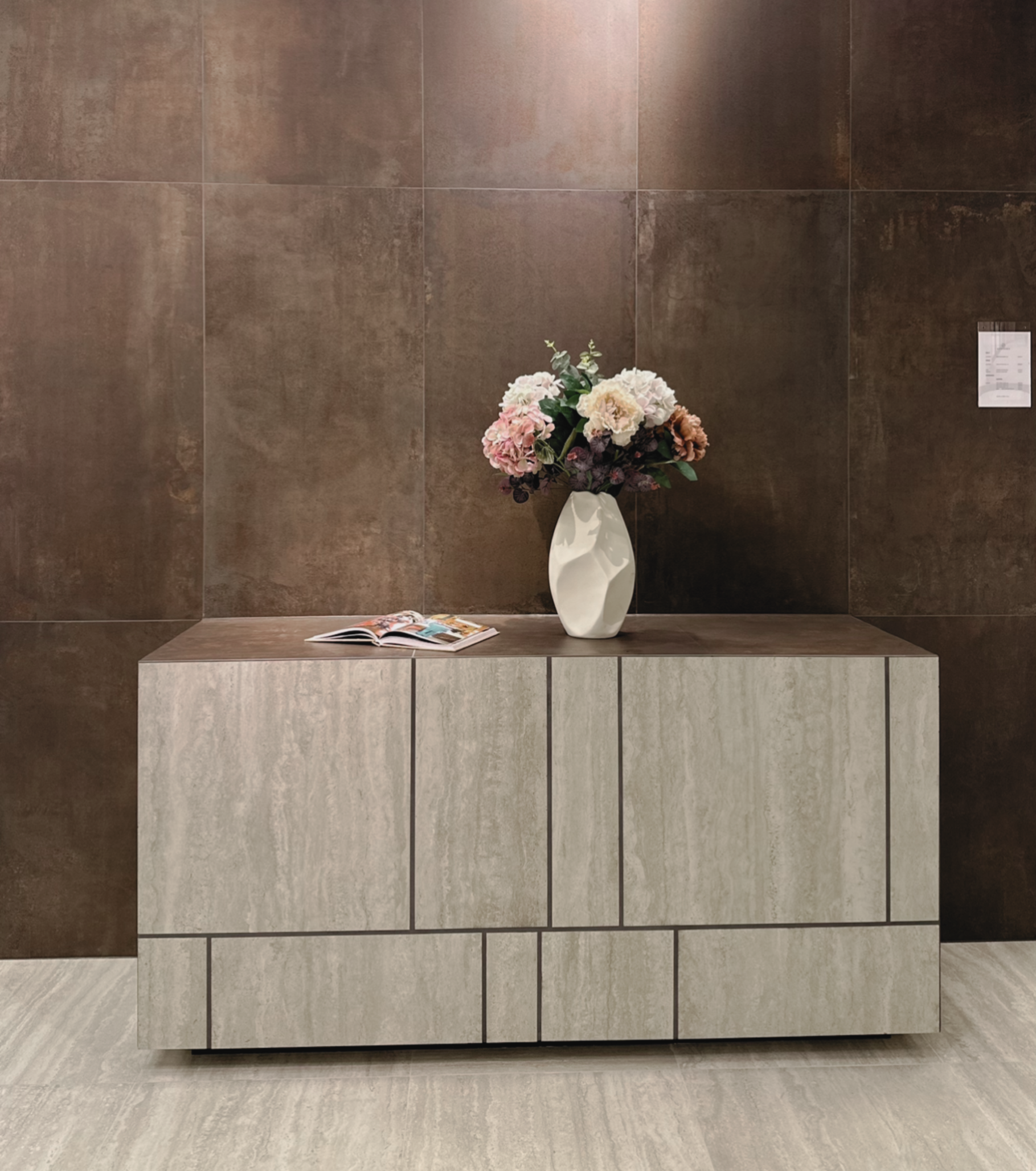 Travertinklädd sideboard mot en vägg i bronsskimrande klinker, del av showroomets styling.