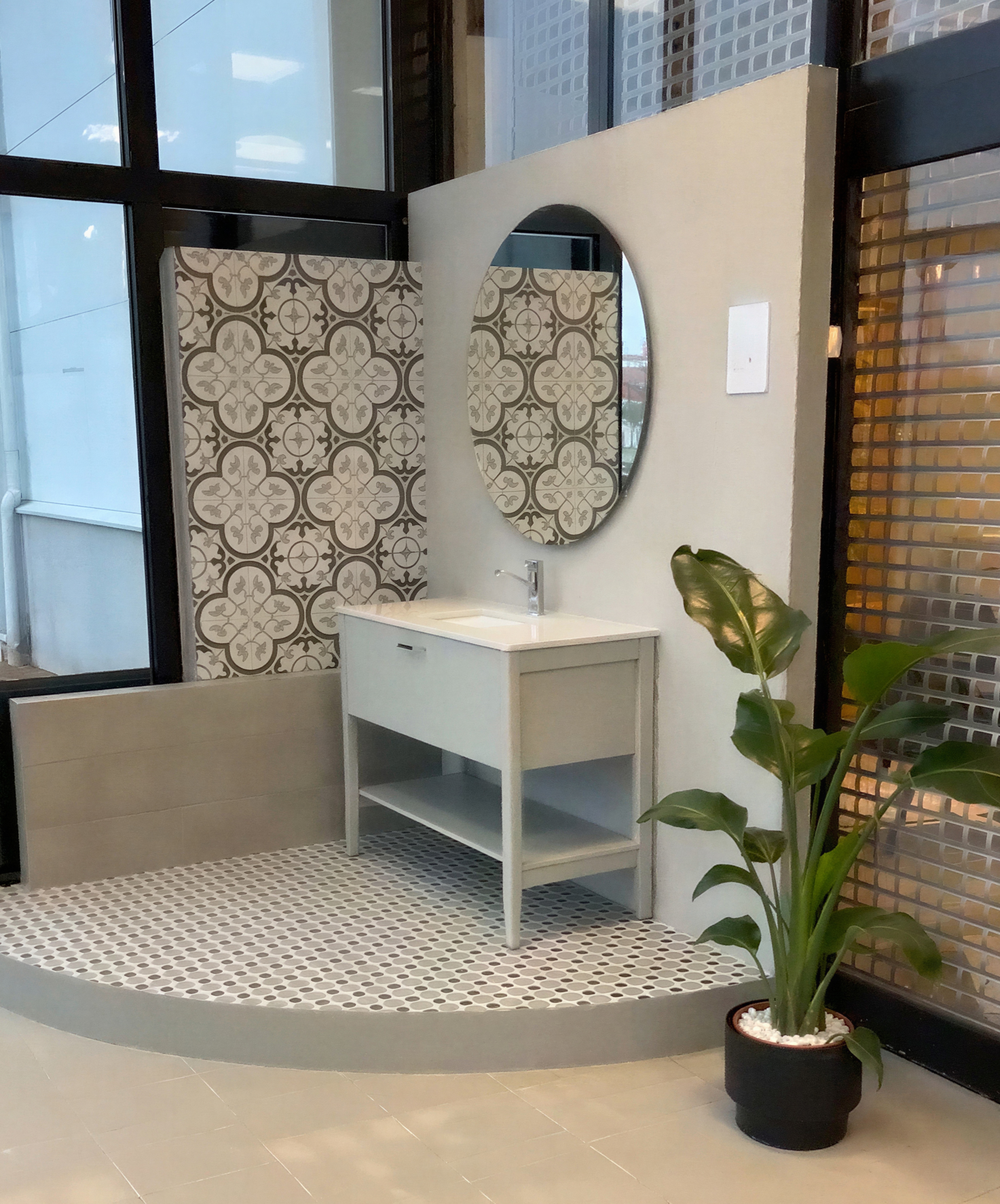 Badrumshörn i HT:s showroom med mönstrad cementkakel, oval spegel och runt mosaikgolv.