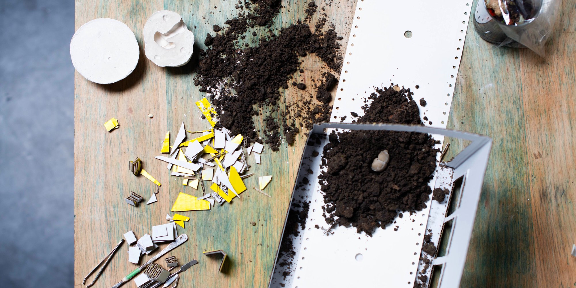 Werkbank beim Figurenbau für THE BUG: Erde, Papierstreifen, gelbe Pappschnipsel und Werkzeug auf einem Holztisch