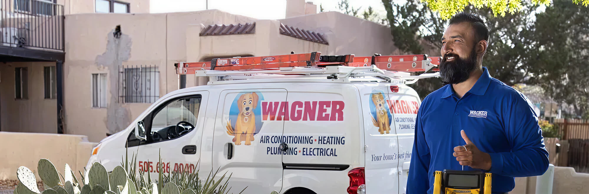 A technician in a blue shirt, standing in front of a Wagner service van equipped with ladders on the roof. The van is labeled with 'Wagner Air Conditioning - Heating - Plumbing - Electrical' and a cartoon dog logo. The technician is holding a multimeter and smiling, with a residential building and cactus plants in the background.