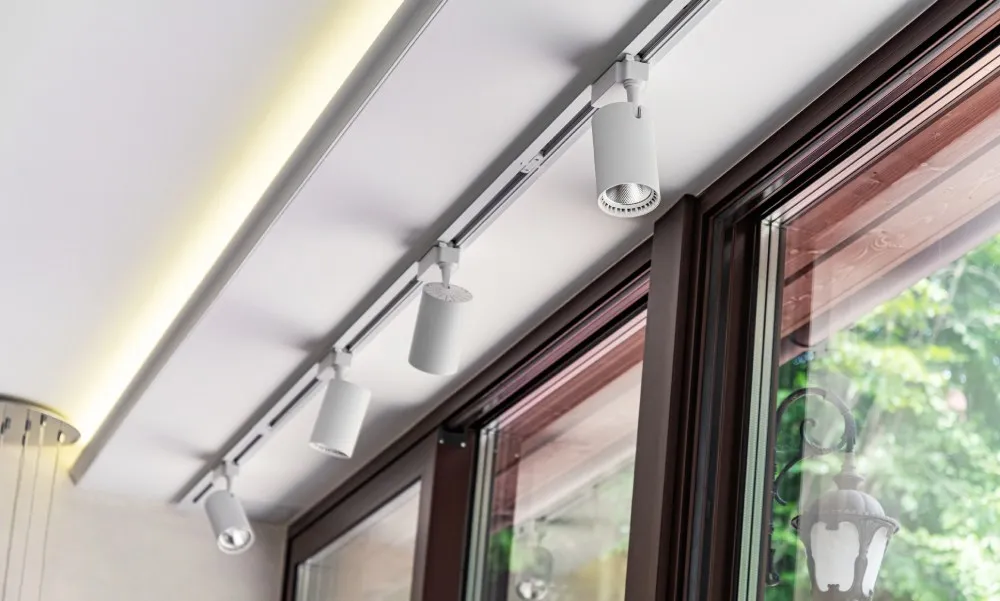 Ceiling-mounted track lighting with multiple spotlights above tall windows.