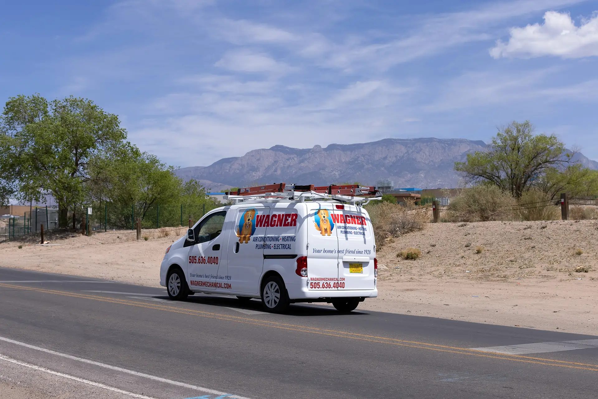 White Wagner service van driving on a desert road with mountains and blue sky in the background.