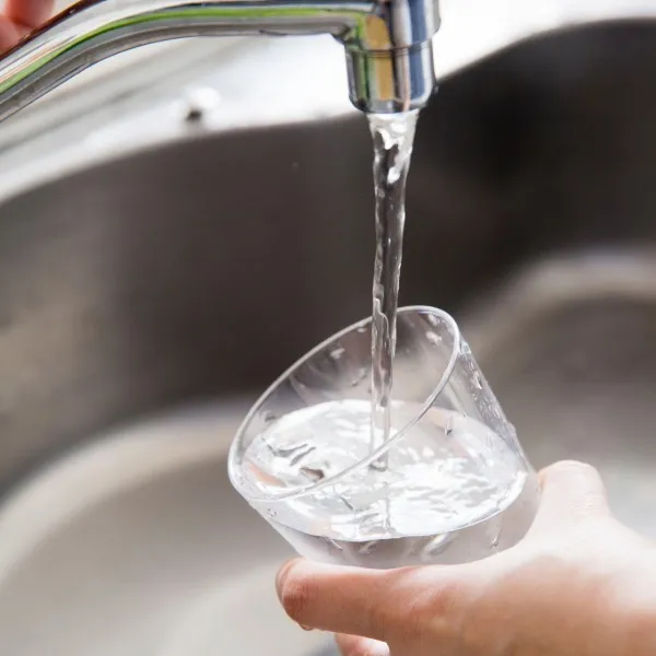 Hand holding a glass under a kitchen faucet filling it with clear water above a sink.