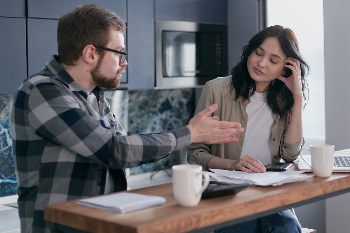 Man gesturing at his wife and talking while they stand at the kitchen counter.