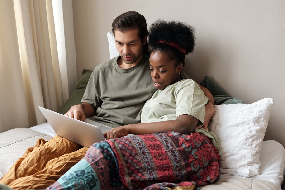 Couple sitting together relaxed on the bed looking at a laptop.