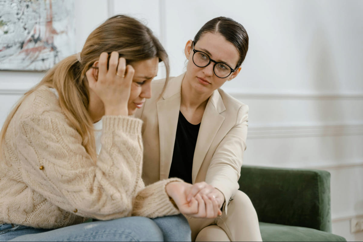 Woman sitting on a couch while a therapist holds her hand for support