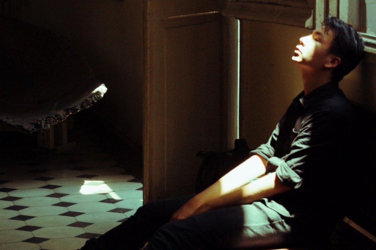 Person sitting on the floor by a window, sunlight on their face as they look upward.