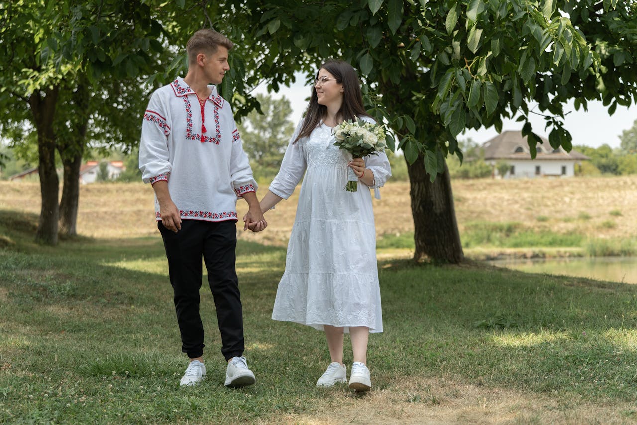 Couple holding hands and walking through a leafy park.