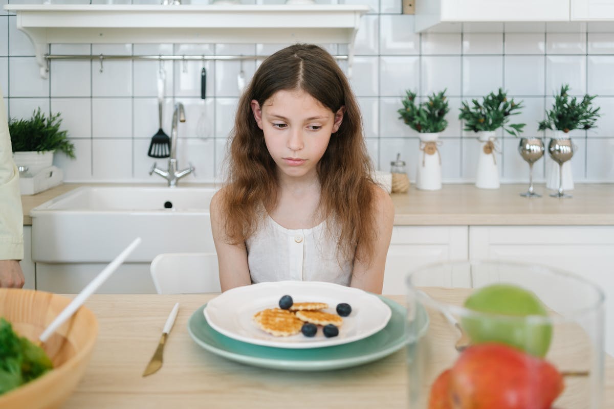 Young woman sitting at a table with an empty plate, looking disappointed.