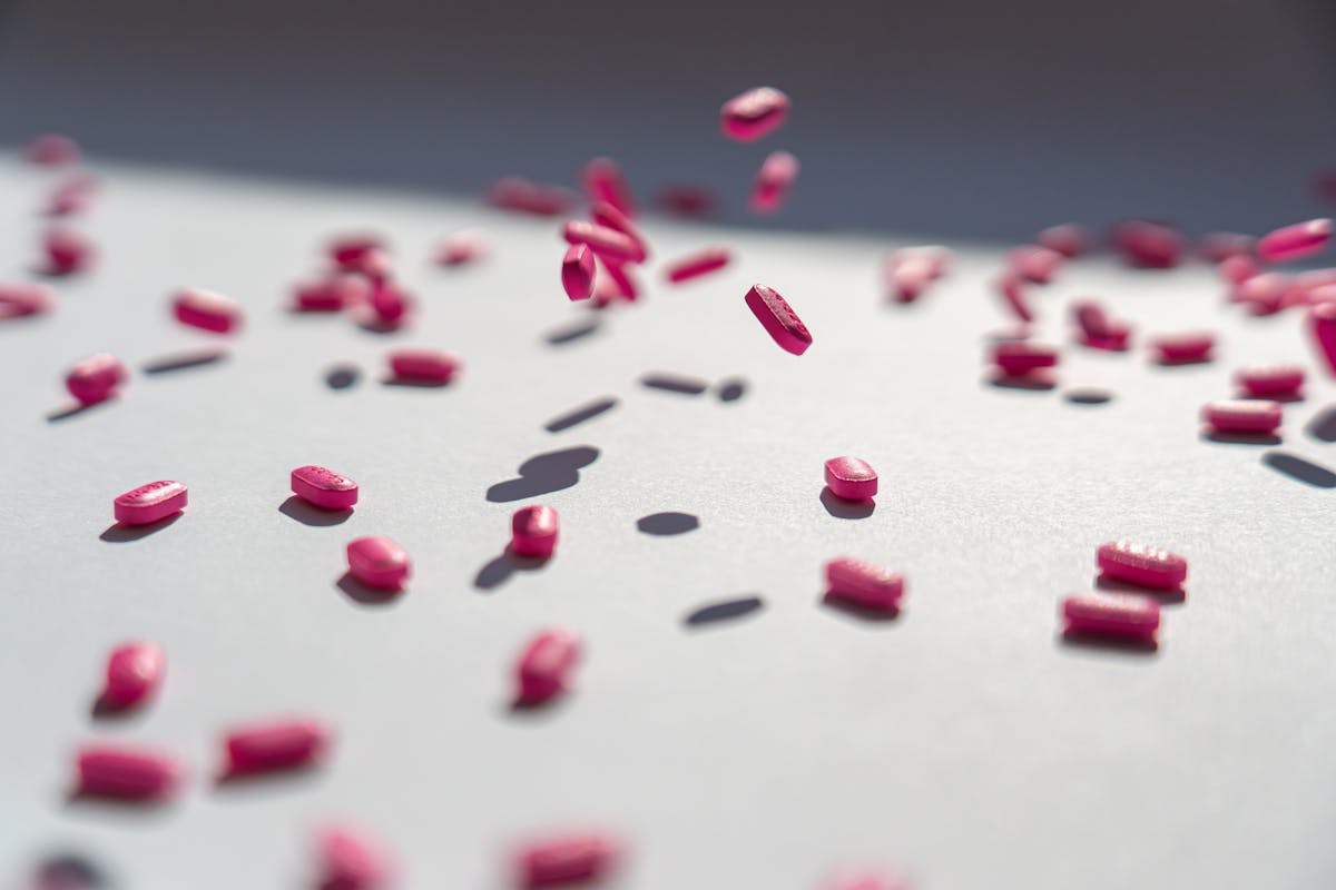 Red and pink tablets scattered and falling on a white surface.