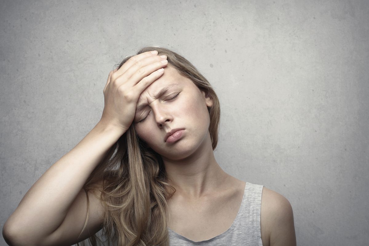A woman with her eyes closed, pressing her hand against her forehead in a gesture