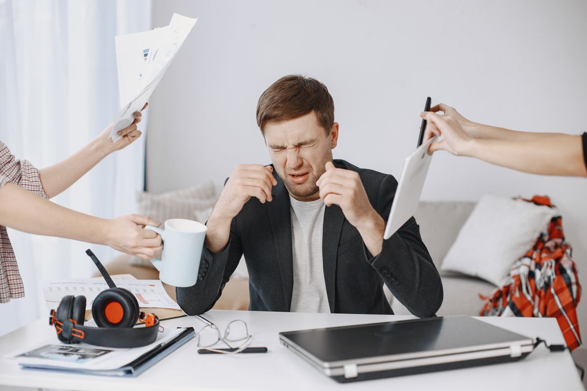  A person overwhelmed with work demands, surrounded by hands holding paperwork, a digital tablet, and a coffee mug