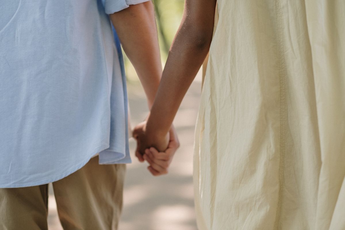 Two individuals holding hands while walking outdoors during a sunny day.