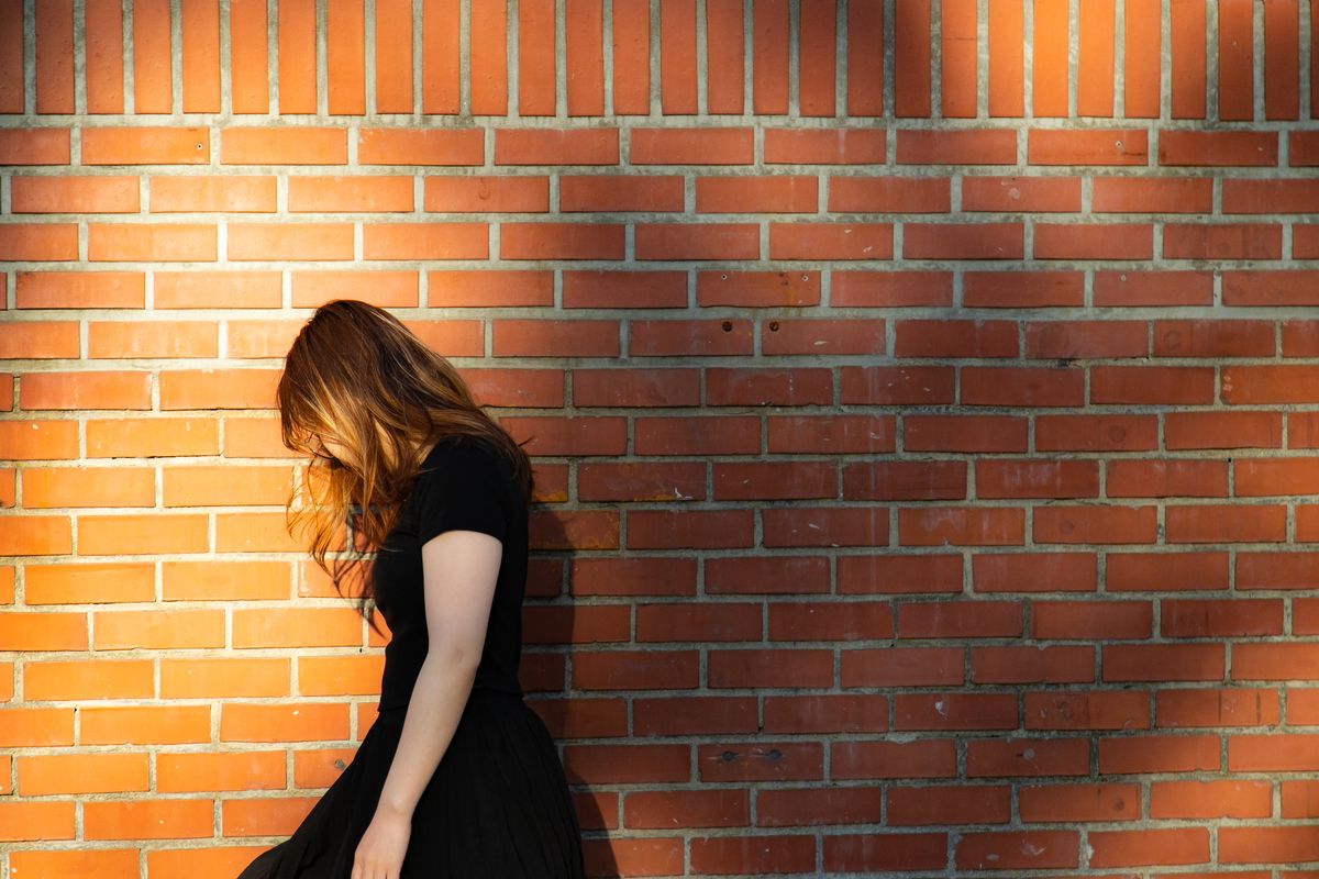 A person standing against a red brick wall.