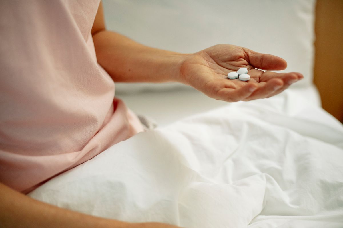 A person's hand holding three small pills.