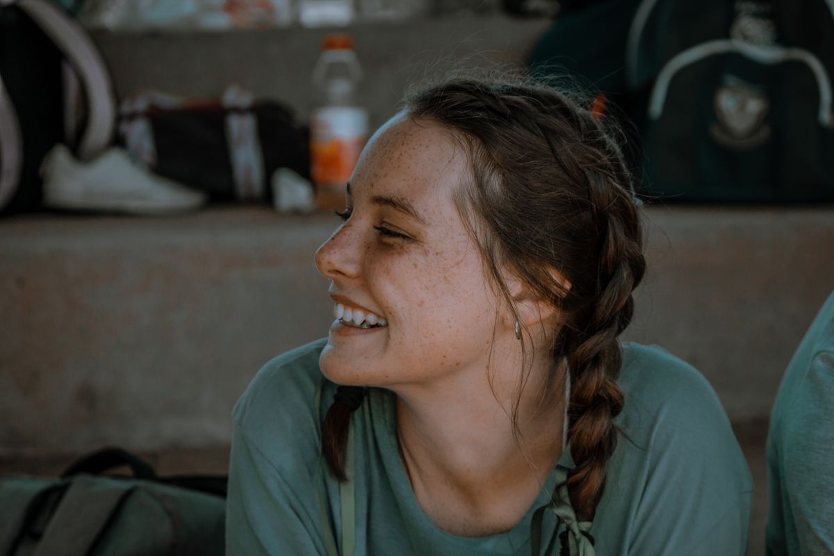 A girl sitting outdoors and smiling with braided hair.