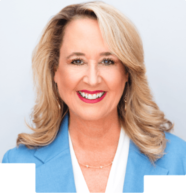 Smiling woman with blonde hair wearing a blue blazer and white blouse against a white background.