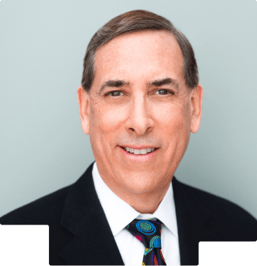 Portrait of a middle-aged man in a suit and colorful tie against a gray background.