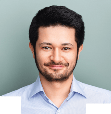 Headshot of a man with short black hair, light beard, and blue shirt smiling against gray background.