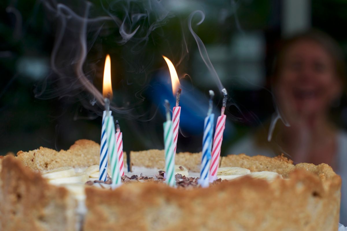 Birthday cake decorated with sliced bananas and several lit striped candles.