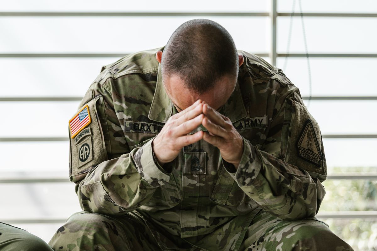 This image shows a person in a army uniform sitting with their head in their hands.