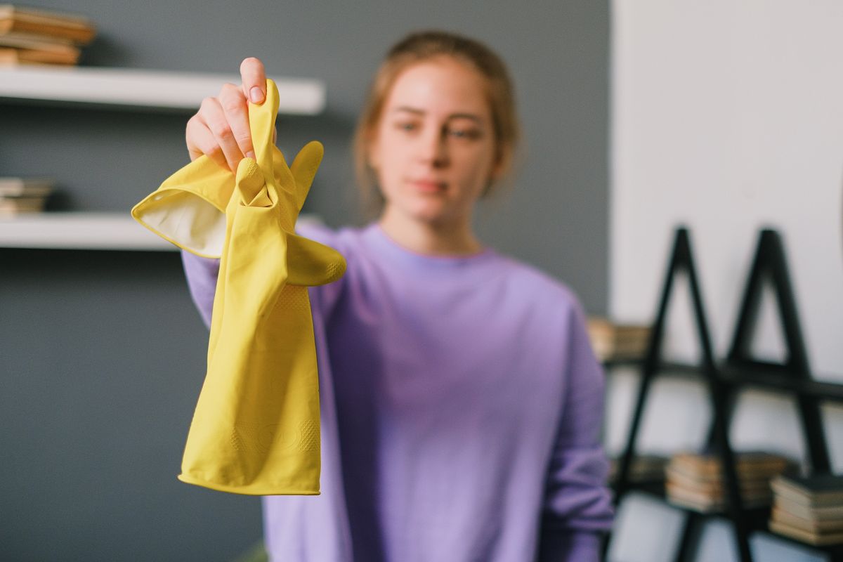 A person holding up a pair of bright yellow latex household gloves.
