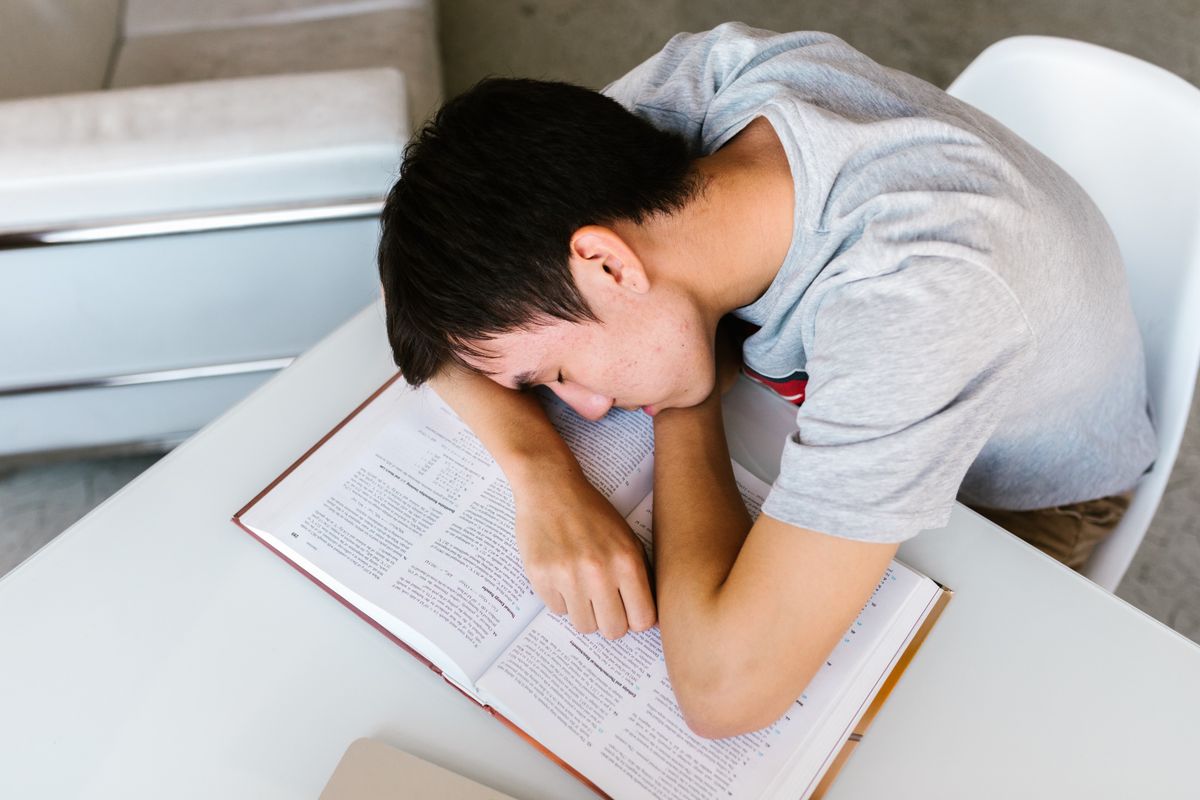 A young person fast asleep with their head resting on an open textbook