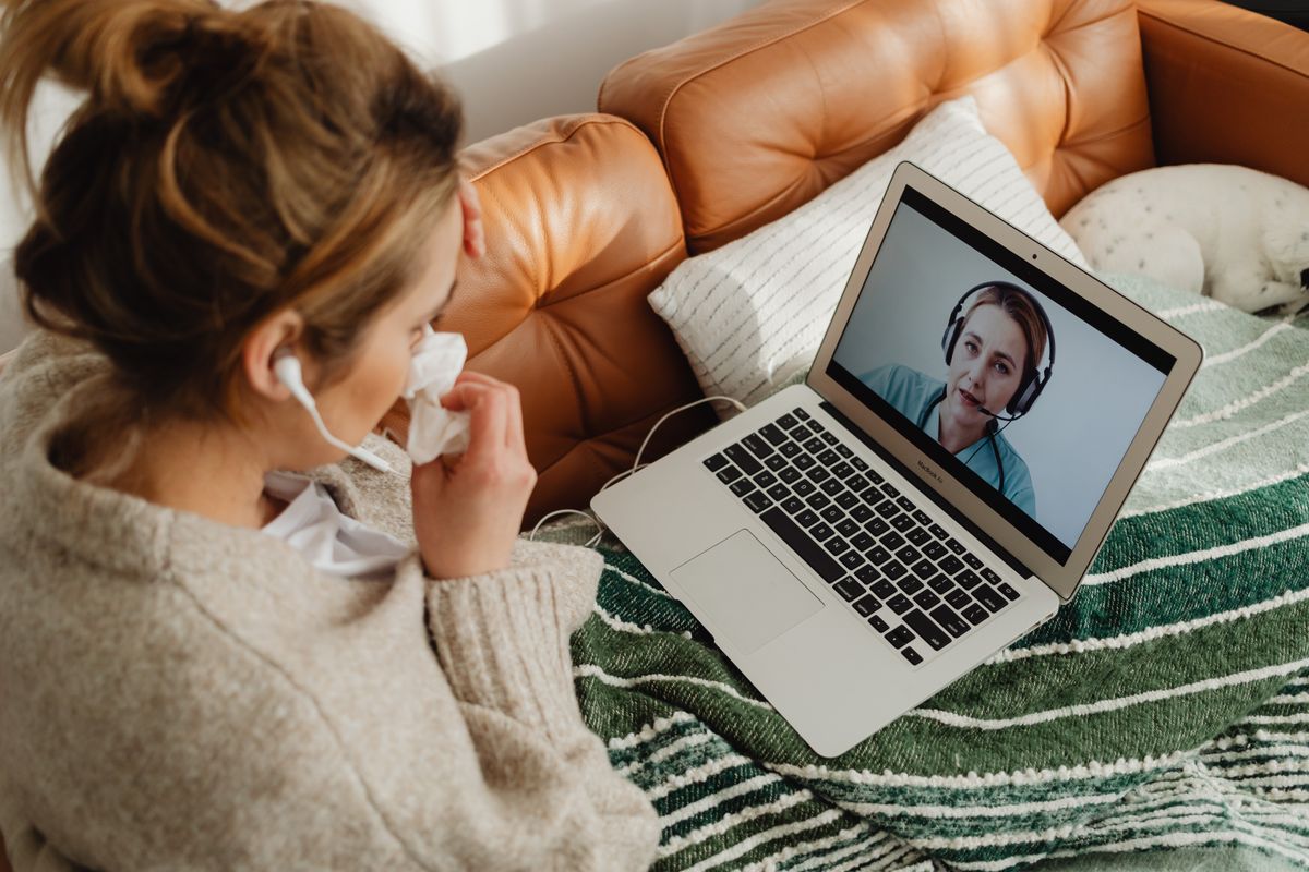 Woman resting on a couch while consulting a doctor via laptop.