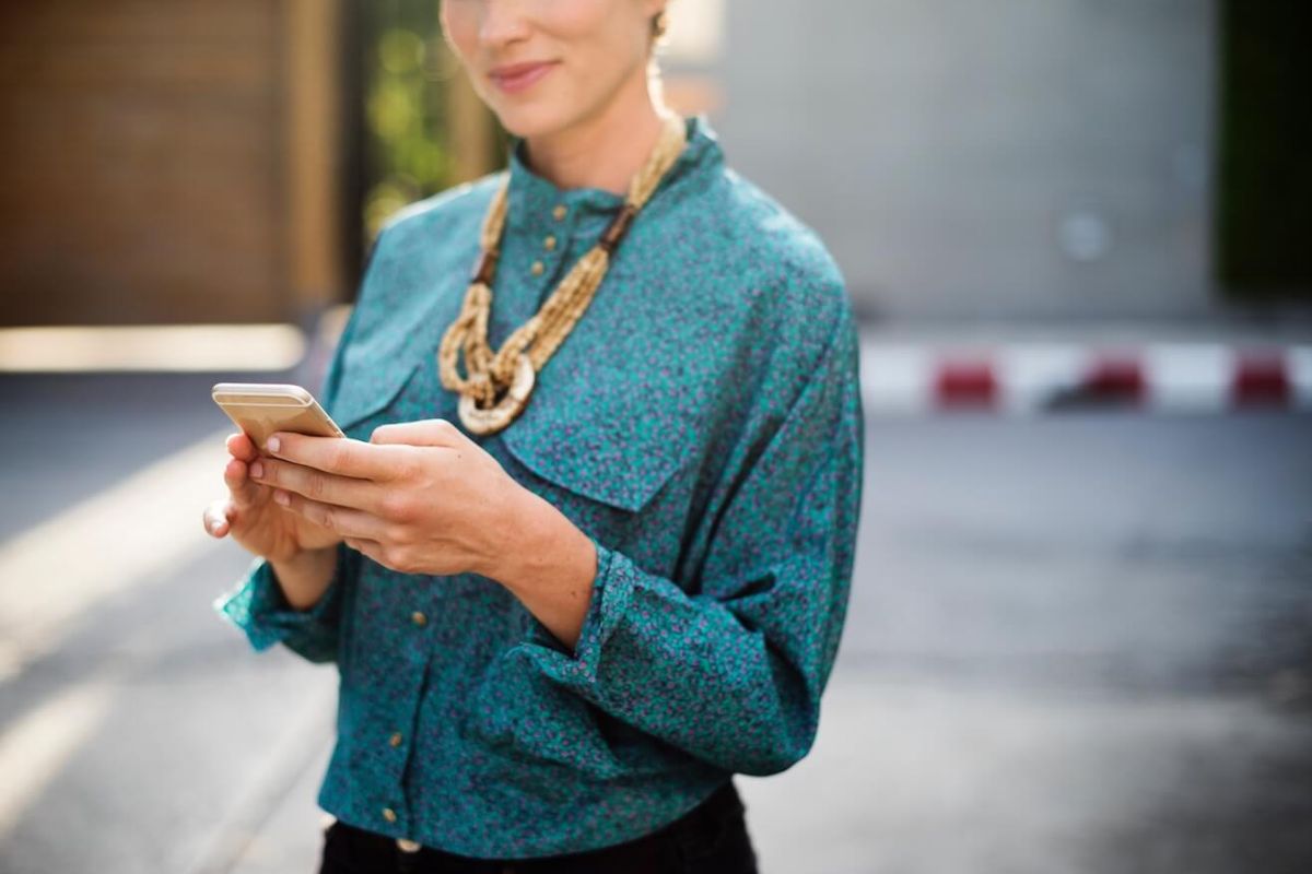 A woman stands outdoors, holding a smartphone in both hands.